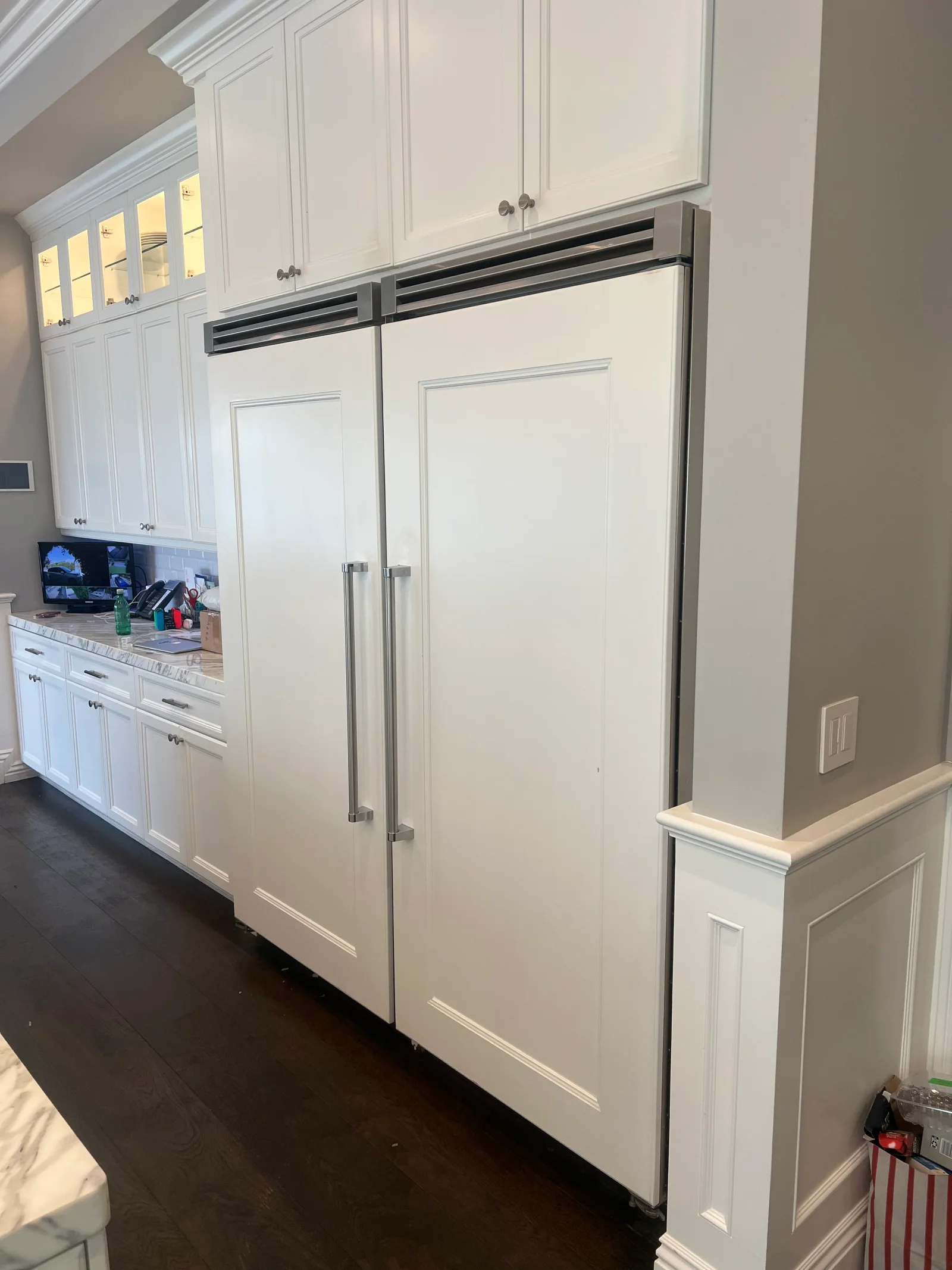 Built-in stainless steel refrigerator with dual sliding doors integrated into white kitchen cabinetry