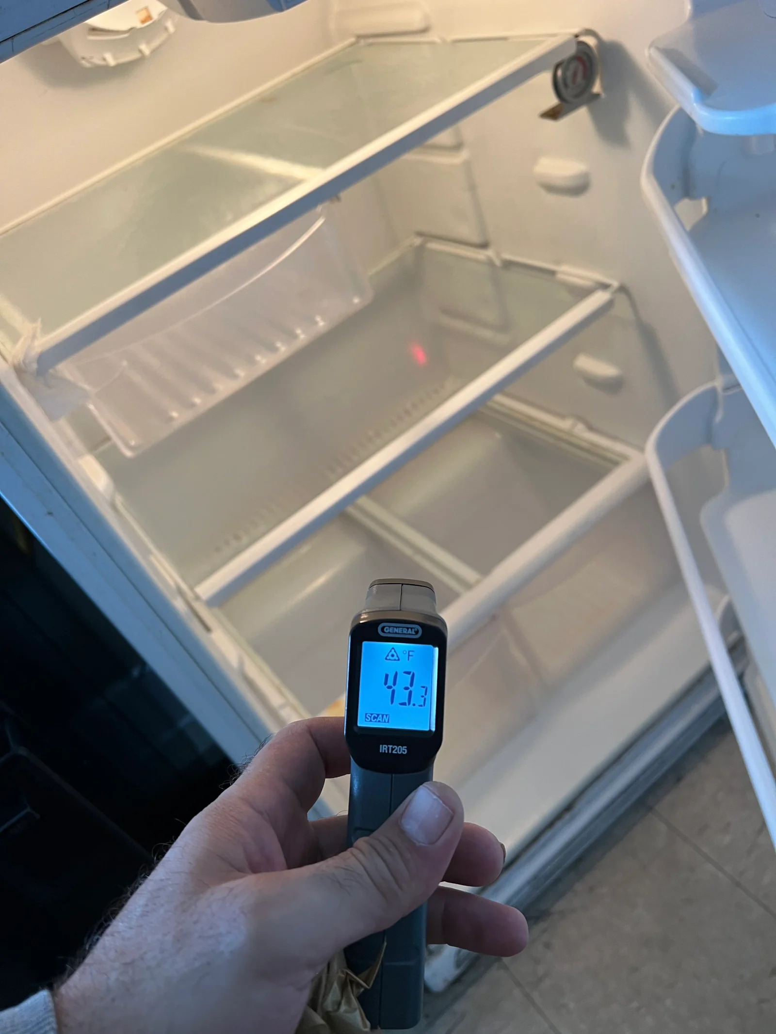 Infrared thermometer reading 47.3°F inside white cooler compartment during diagnostic testing
