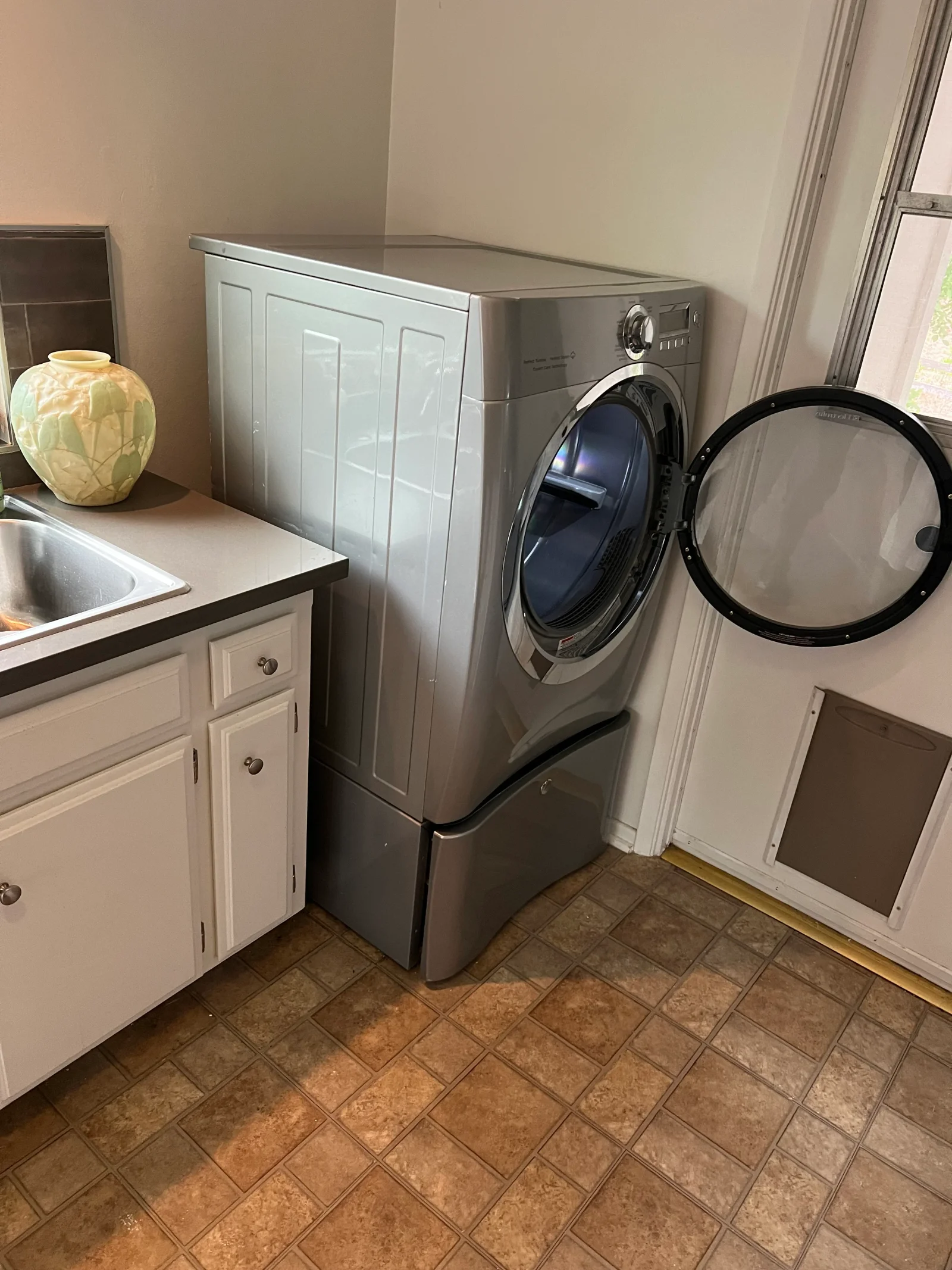 Stainless steel front-load washer and dryer installed in white cabinet laundry room with tile flooring