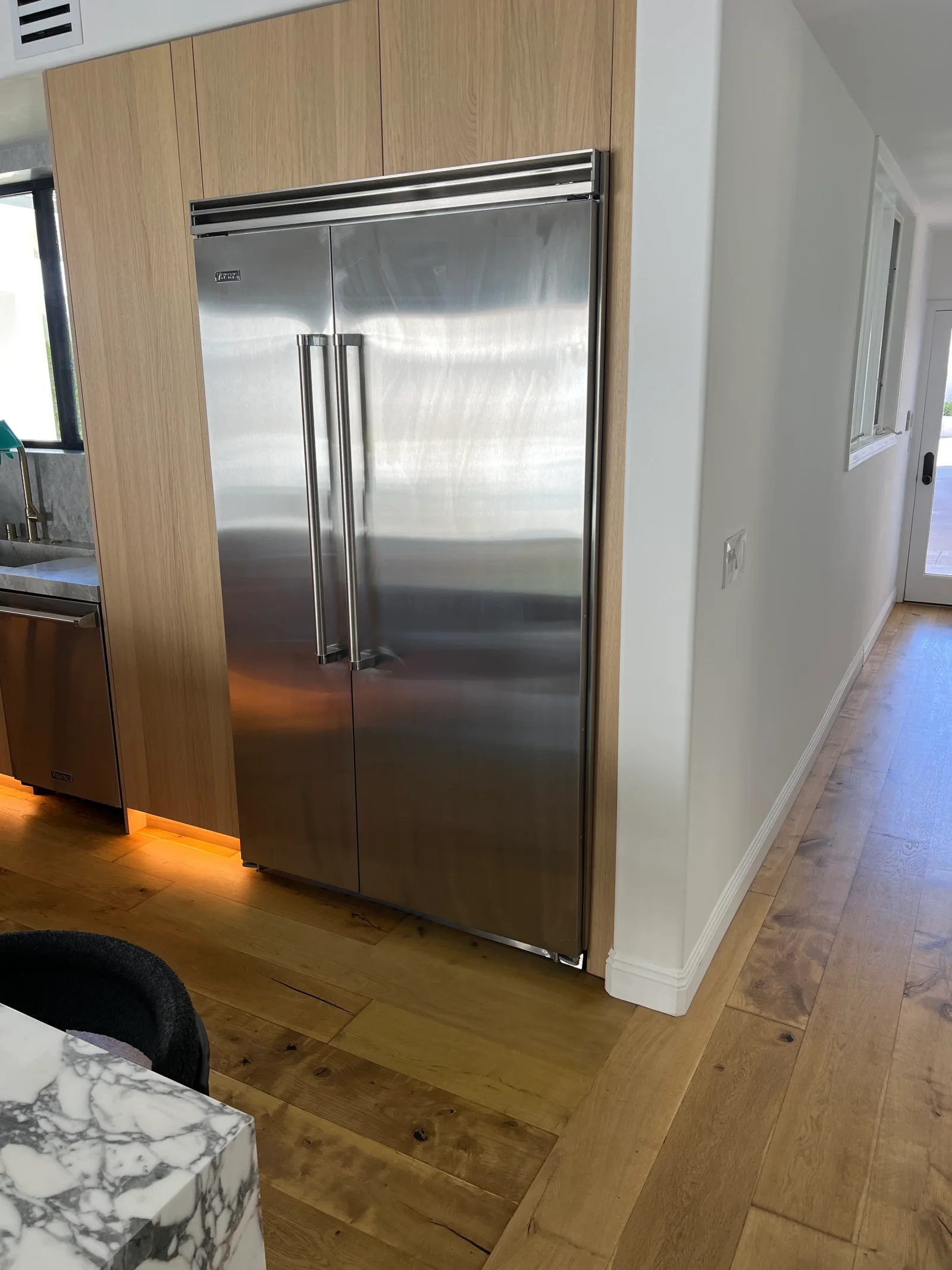 Stainless steel built-in refrigerator installed in light wood cabinetry with dual doors and chrome handles