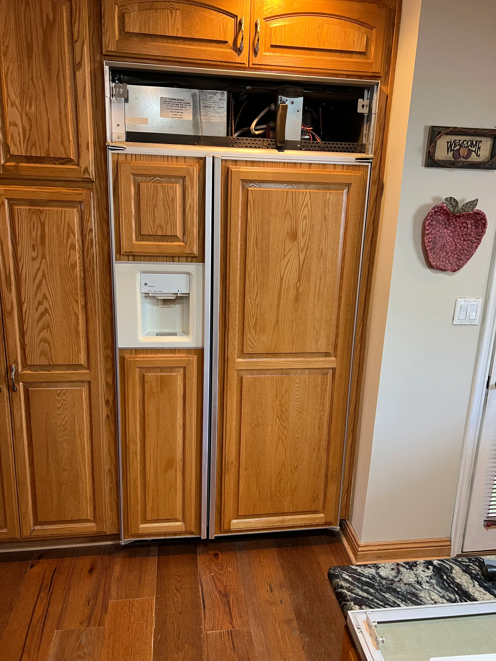 Stainless steel refrigerator with ice maker installed in oak wood cabinet enclosure