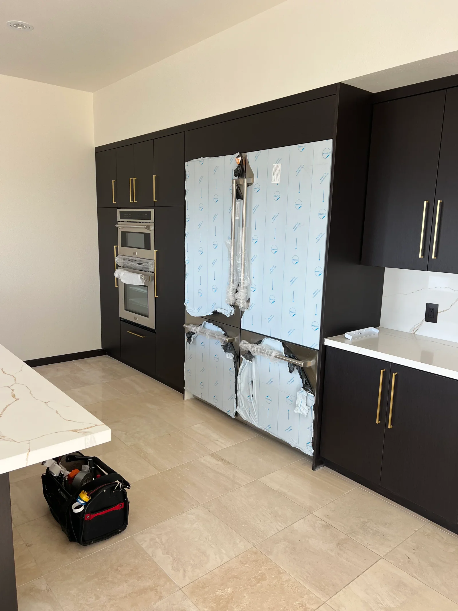 Stainless steel French door refrigerator with protective covering in black cabinet kitchen