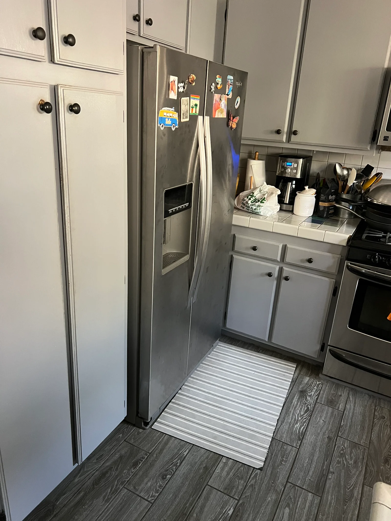 Stainless steel side-by-side refrigerator with ice dispenser in white kitchen with subway tile and wood flooring